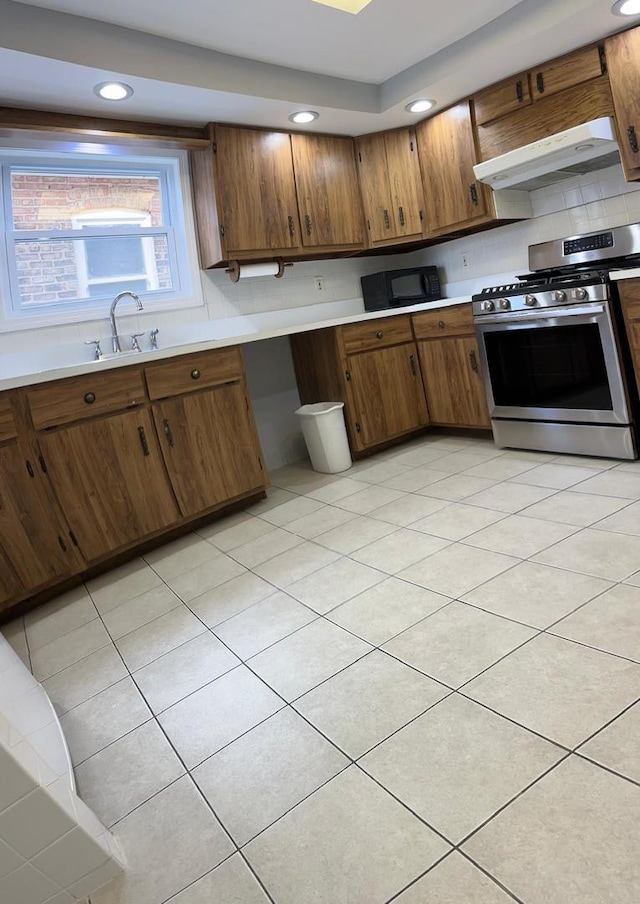 kitchen featuring tasteful backsplash, range hood, stainless steel stove, light tile patterned floors, and sink