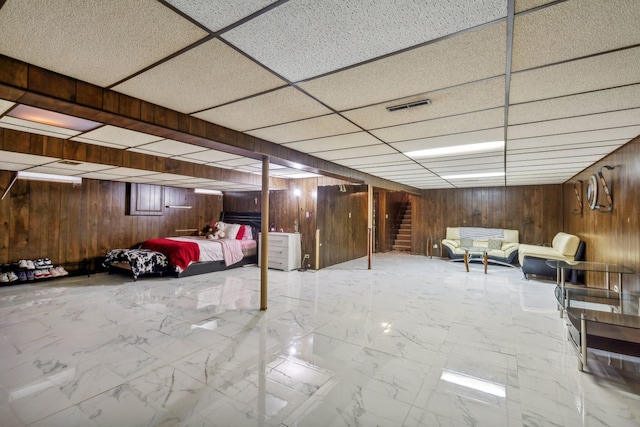 basement featuring a paneled ceiling and wooden walls