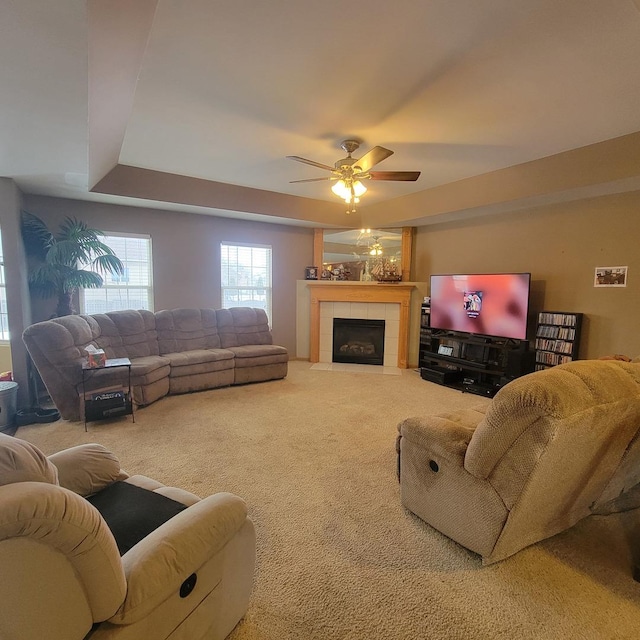 living room with ceiling fan, carpet flooring, a raised ceiling, and a tile fireplace