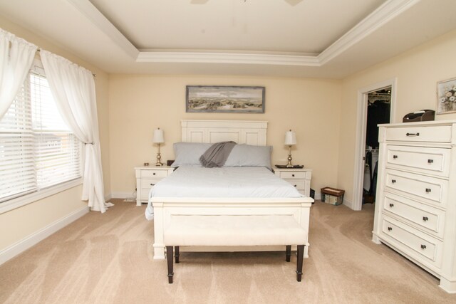 bedroom featuring light carpet, a tray ceiling, and a walk in closet