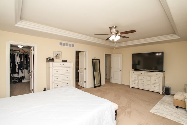 carpeted bedroom with a raised ceiling, a walk in closet, a closet, and ceiling fan