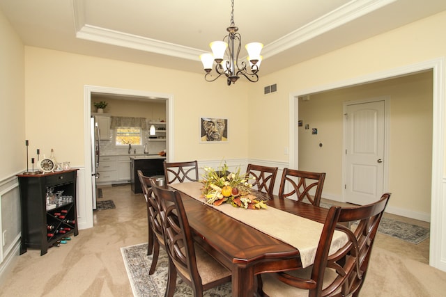 carpeted dining area featuring a notable chandelier, a raised ceiling, and ornamental molding