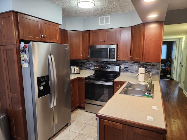 kitchen with appliances with stainless steel finishes, a textured ceiling, decorative backsplash, sink, and light hardwood / wood-style flooring