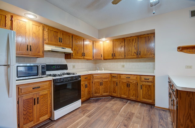 kitchen featuring wood-type flooring, white appliances, tasteful backsplash, and sink