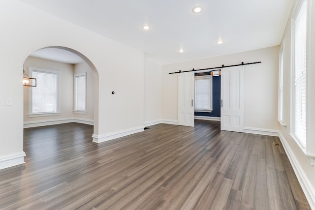 spare room with a barn door and dark wood-type flooring