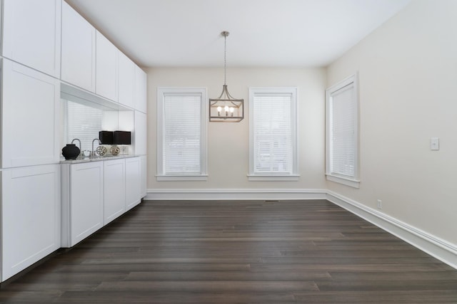 unfurnished dining area featuring a chandelier, a healthy amount of sunlight, and dark hardwood / wood-style floors