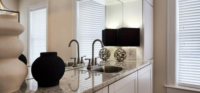 kitchen featuring white cabinets, light stone countertops, and sink