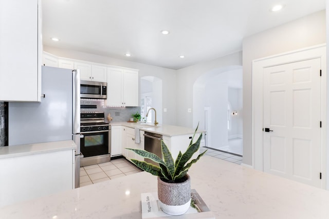 kitchen with stainless steel appliances, light tile patterned floors, tasteful backsplash, white cabinetry, and sink