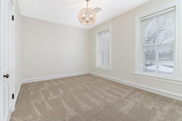 carpeted empty room with an inviting chandelier