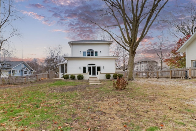 back house at dusk featuring a lawn and a sunroom