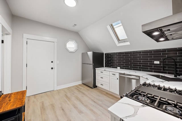 kitchen featuring stainless steel appliances, lofted ceiling with skylight, light hardwood / wood-style floors, and exhaust hood