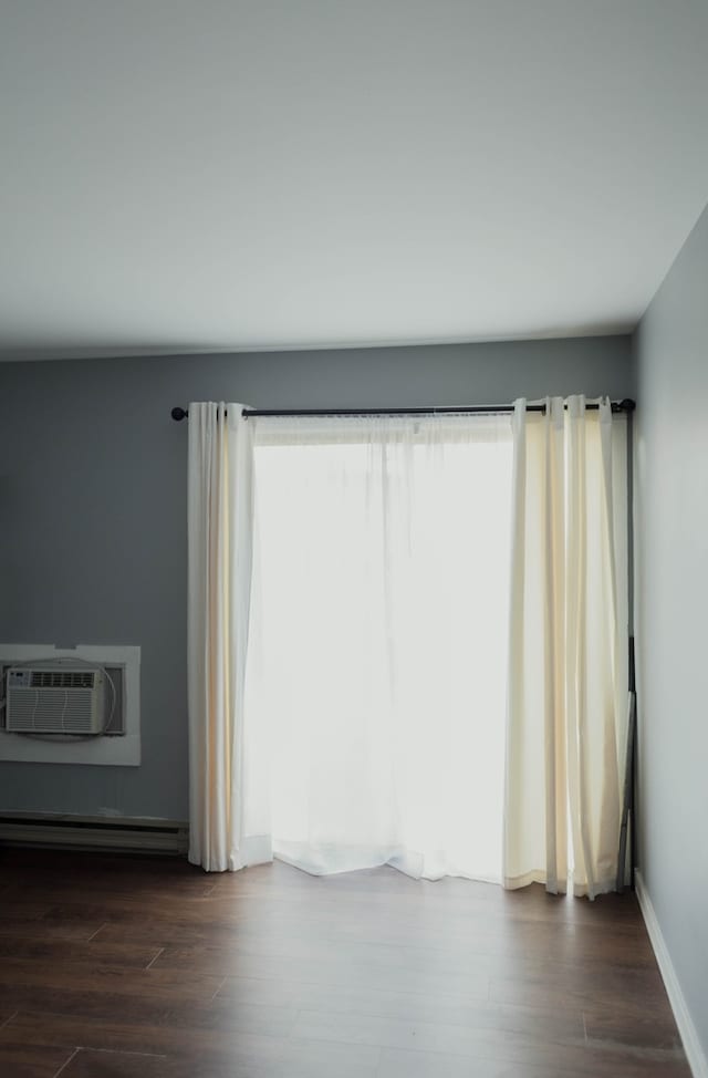 unfurnished room with dark hardwood / wood-style floors, an AC wall unit, and baseboard heating