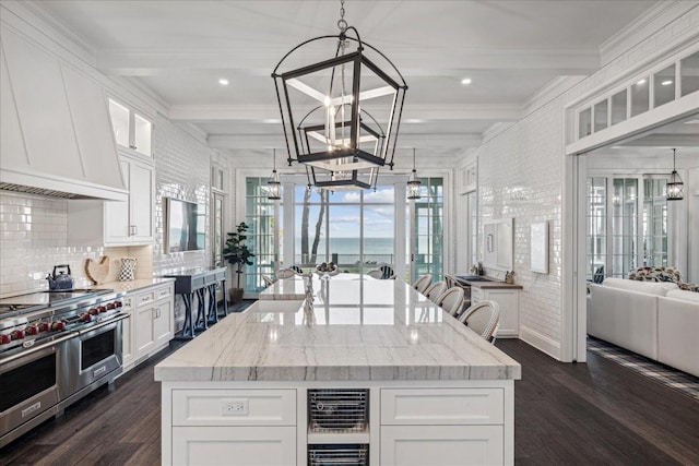 kitchen featuring premium range hood, an inviting chandelier, hanging light fixtures, range with two ovens, and white cabinets