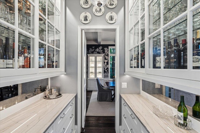 bar with white cabinetry, ornamental molding, dark hardwood / wood-style flooring, and light stone counters