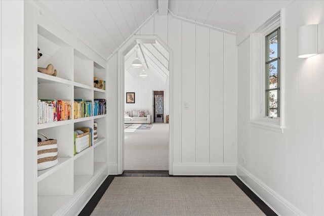 corridor with built in shelves, lofted ceiling, and wooden walls