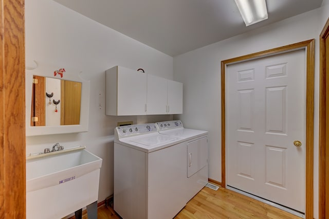 laundry area featuring sink, light hardwood / wood-style flooring, washer and clothes dryer, and cabinets