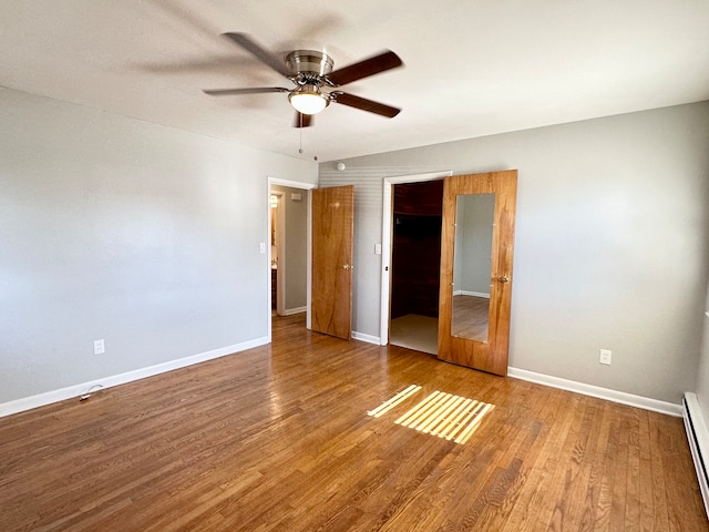 unfurnished bedroom with ceiling fan, baseboard heating, hardwood / wood-style floors, a walk in closet, and a closet