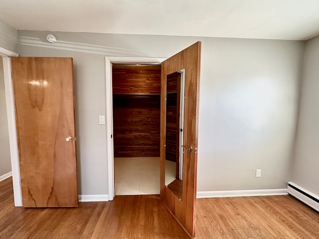 unfurnished bedroom featuring light wood-type flooring, a closet, and a baseboard heating unit