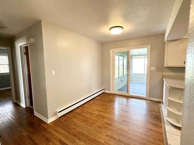 unfurnished dining area with a textured ceiling, a baseboard radiator, and wood-type flooring