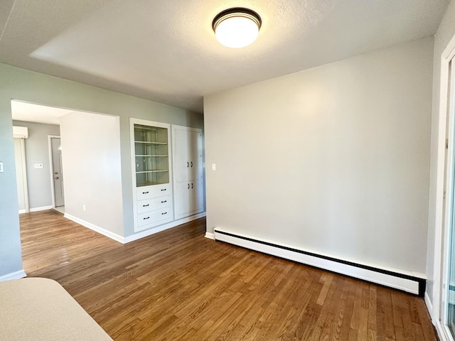 unfurnished room with a textured ceiling, hardwood / wood-style floors, built in features, and a baseboard heating unit