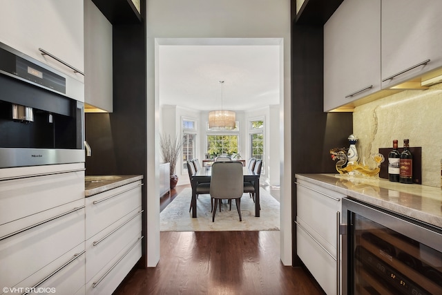 kitchen featuring oven, dark hardwood / wood-style flooring, hanging light fixtures, beverage cooler, and light stone counters