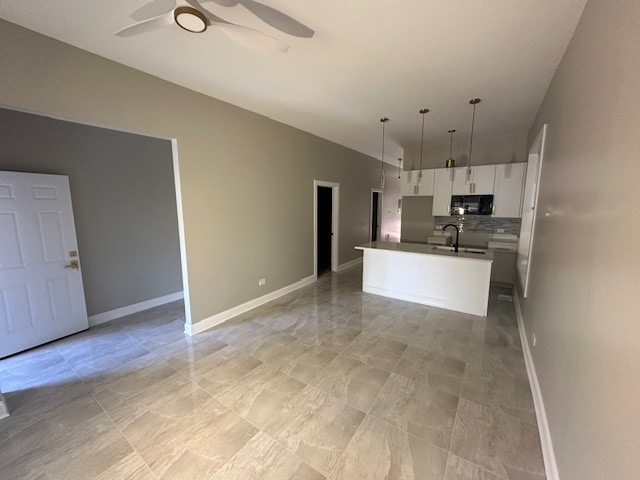 kitchen with white cabinetry, ceiling fan, decorative light fixtures, and an island with sink