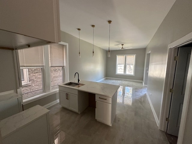 kitchen featuring ceiling fan, white cabinetry, sink, decorative light fixtures, and light stone counters