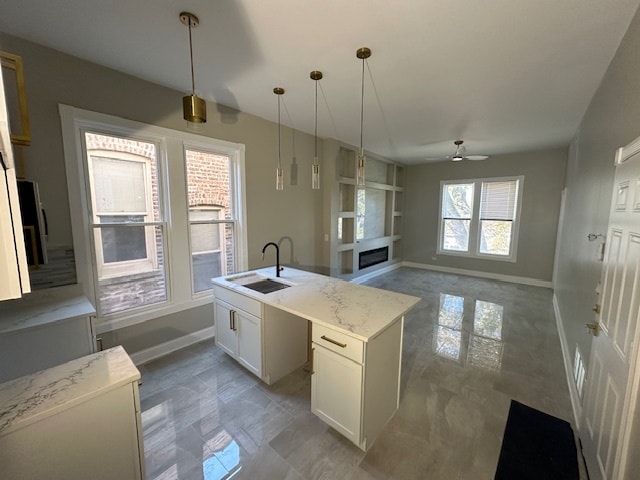 kitchen featuring white cabinets, ceiling fan, an island with sink, pendant lighting, and sink