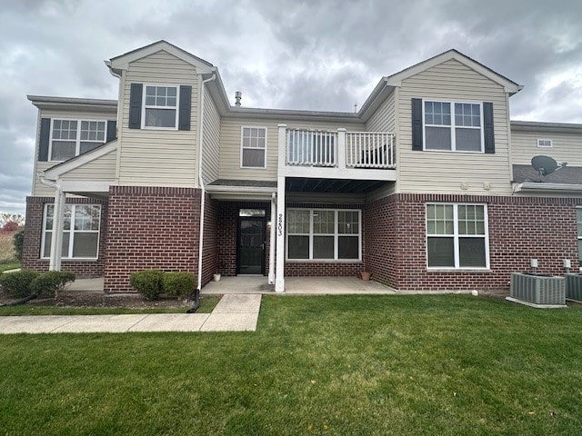 view of front of home with central air condition unit, a front yard, a patio, and a balcony