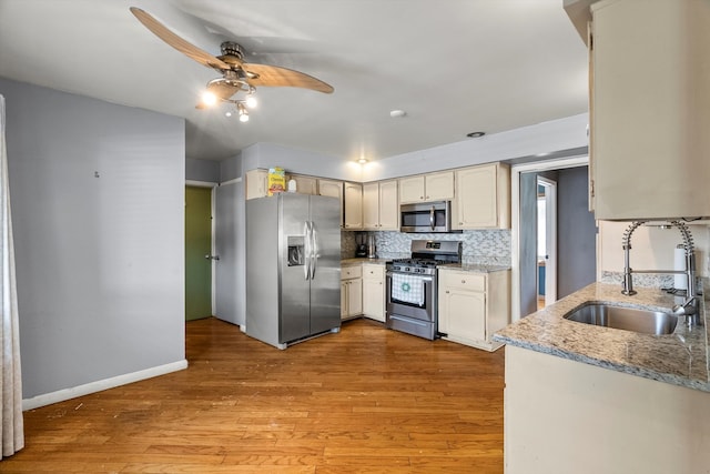 kitchen featuring decorative backsplash, ceiling fan, appliances with stainless steel finishes, light hardwood / wood-style flooring, and sink