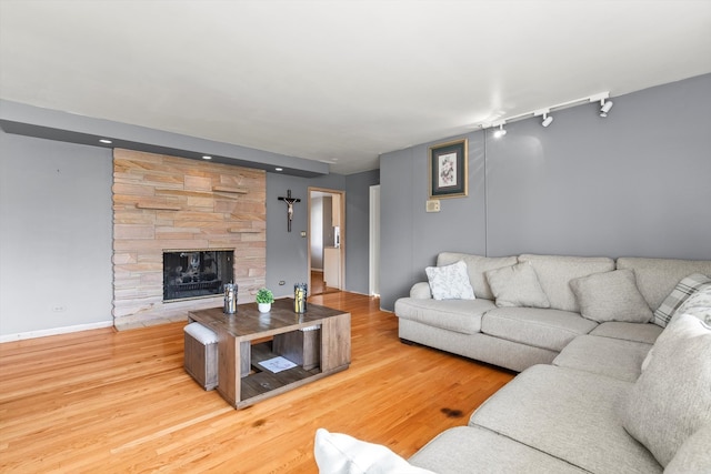 living room with hardwood / wood-style flooring, track lighting, and a stone fireplace