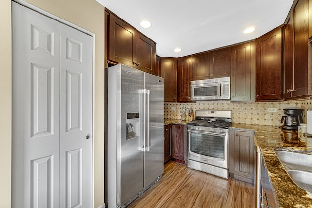 kitchen featuring decorative backsplash, stainless steel appliances, dark stone counters, sink, and light wood-type flooring