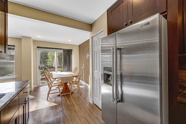 kitchen with dark stone countertops, high quality fridge, dark brown cabinets, and light wood-type flooring