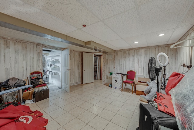 basement with light tile patterned floors, a drop ceiling, and wooden walls