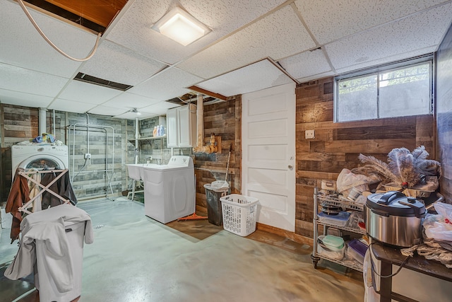 basement with a paneled ceiling, wooden walls, and washer and dryer