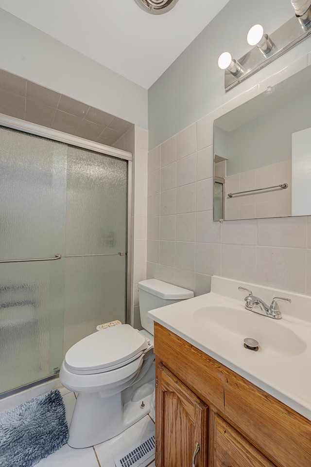 bathroom featuring a shower with shower door, toilet, tile walls, vanity, and tile patterned flooring