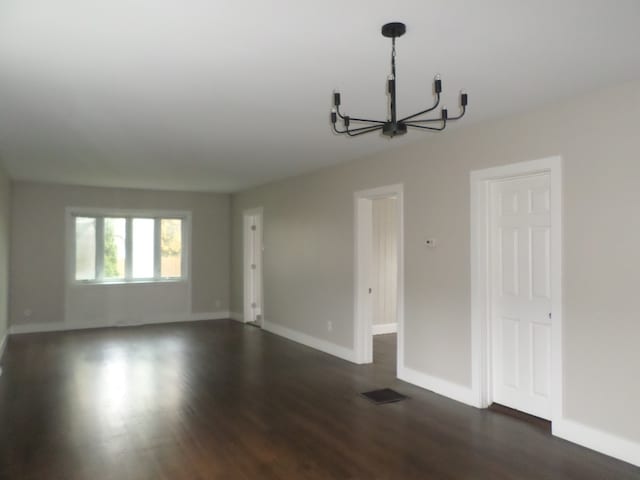 empty room with dark wood-type flooring and a chandelier