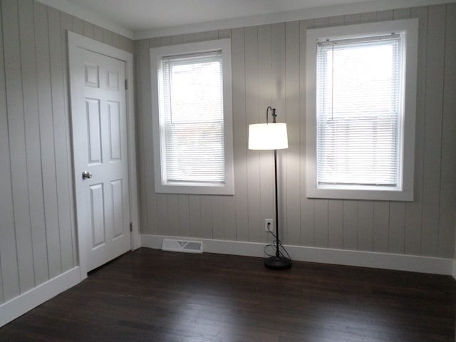 empty room featuring crown molding, dark hardwood / wood-style floors, a healthy amount of sunlight, and wood walls