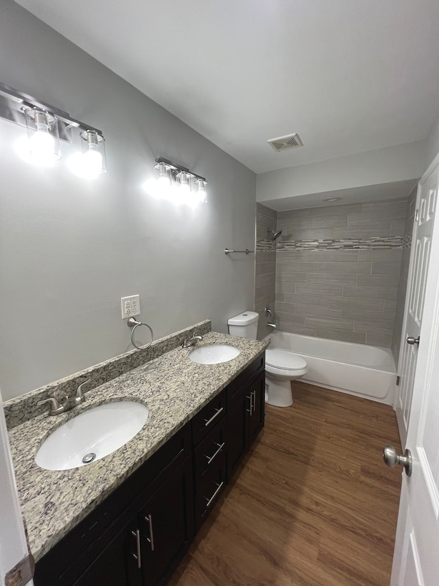 full bathroom featuring vanity, tiled shower / bath combo, hardwood / wood-style flooring, and toilet