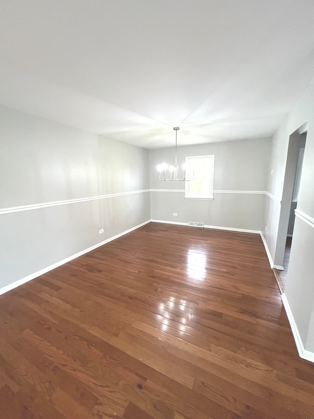 unfurnished room featuring an inviting chandelier and dark wood-type flooring