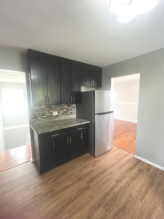 kitchen with decorative backsplash, hardwood / wood-style floors, dark stone countertops, and stainless steel refrigerator