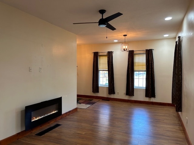 unfurnished living room featuring ceiling fan with notable chandelier and dark hardwood / wood-style flooring