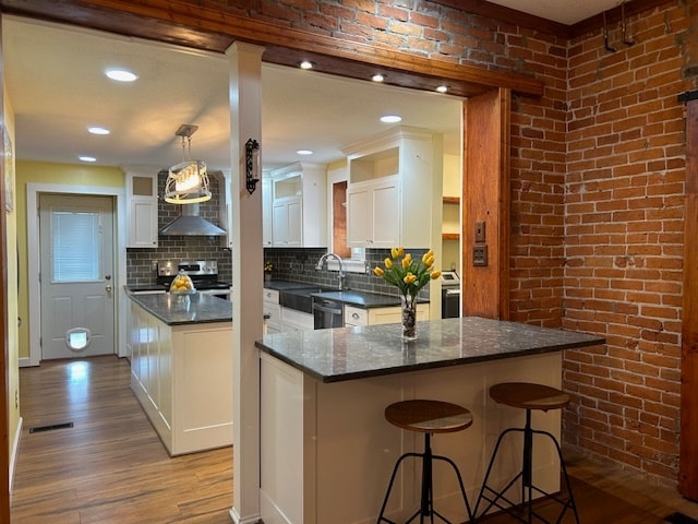 kitchen with electric stove, a kitchen breakfast bar, white cabinetry, light hardwood / wood-style floors, and pendant lighting