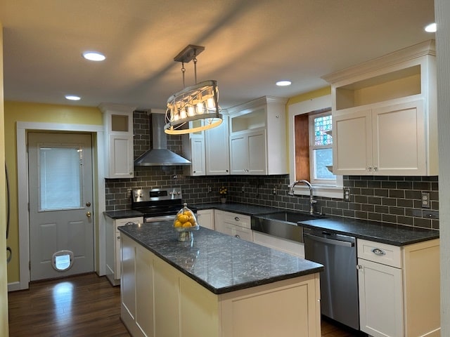 kitchen with wall chimney range hood, a kitchen island, appliances with stainless steel finishes, white cabinetry, and sink