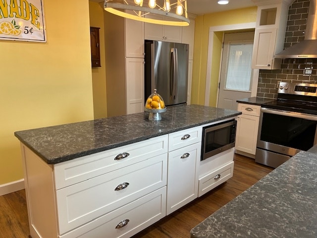 kitchen featuring appliances with stainless steel finishes, wall chimney range hood, pendant lighting, and white cabinets