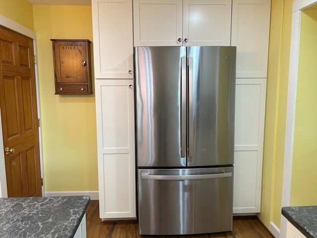 kitchen featuring dark hardwood / wood-style flooring, stainless steel fridge, white cabinetry, and dark stone counters