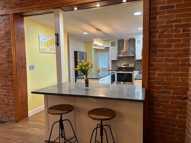 kitchen featuring wall chimney range hood, hanging light fixtures, dark hardwood / wood-style flooring, appliances with stainless steel finishes, and white cabinetry