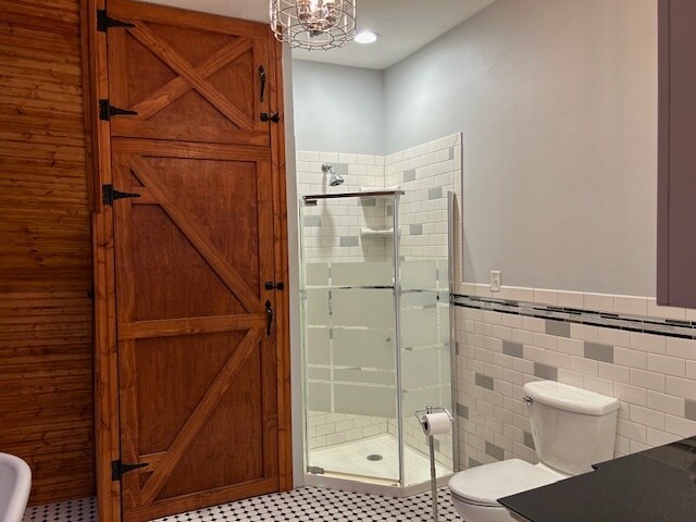 bathroom with tile walls, a shower with shower door, toilet, and tile patterned flooring