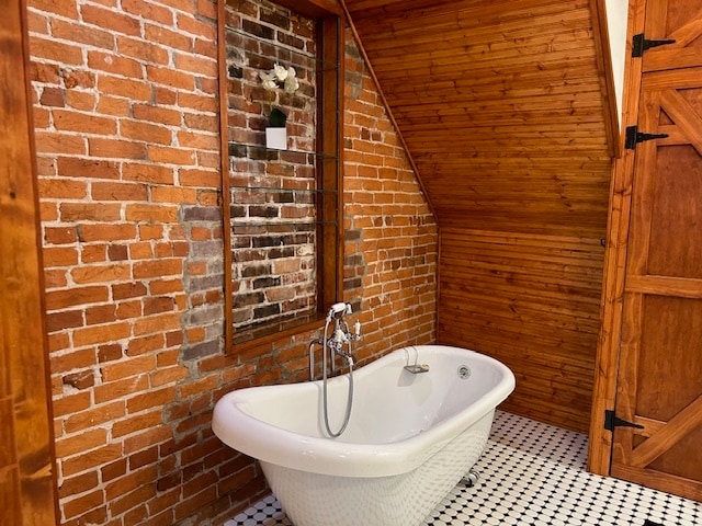 bathroom featuring a tub to relax in, brick wall, vaulted ceiling, and tile patterned flooring