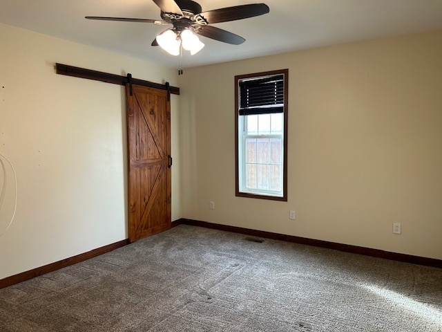 carpeted empty room with a barn door and ceiling fan